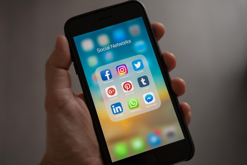 Social media icons on a phone screen. A hand is holding the phone but the person is out of frame.