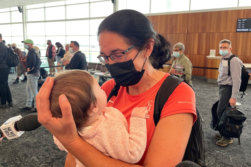 A woman wearing a black face mask holds a baby