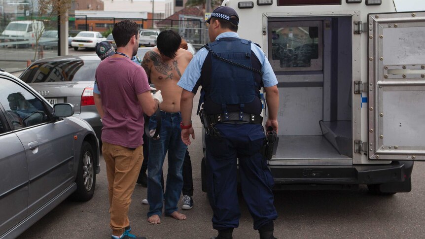 Police speak to a shirtless man following his arrest for drug importation and manufacturing offences.