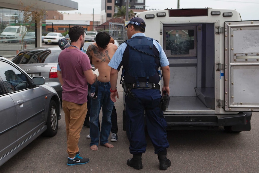 Police speak to a shirtless man following his arrest for drug importation and manufacturing offences.