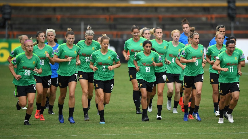 The entire Matildas squad, in training kit, jog around the oval.