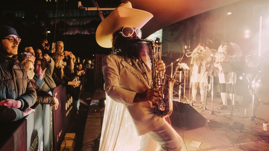 Costa wears a giant hat as he plays sax onstage.
