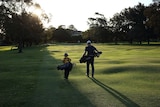 A child and man walk onto a golf course