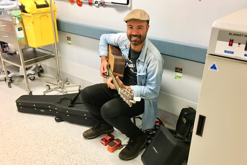 Musician playing a guitar in a hallway.