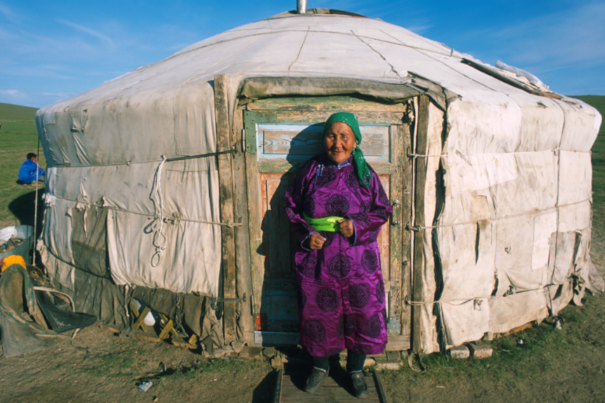 An elderly woman stands outside her home in Mongolia.