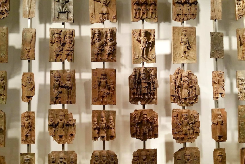 A number of sculptured plaques depicting soldiers arranged in a grid hanging in front of a wall.