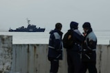 Rescue personnel watch on a pier as a navy ship sails near the crash site of the Russian military aircraft.