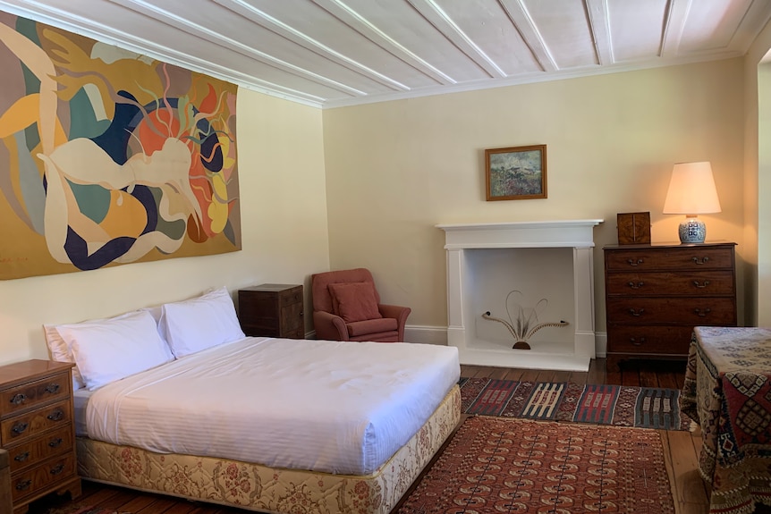 A simple, heritage style bedroom featuring a lot of rugs, a queen bed and a large artwork.