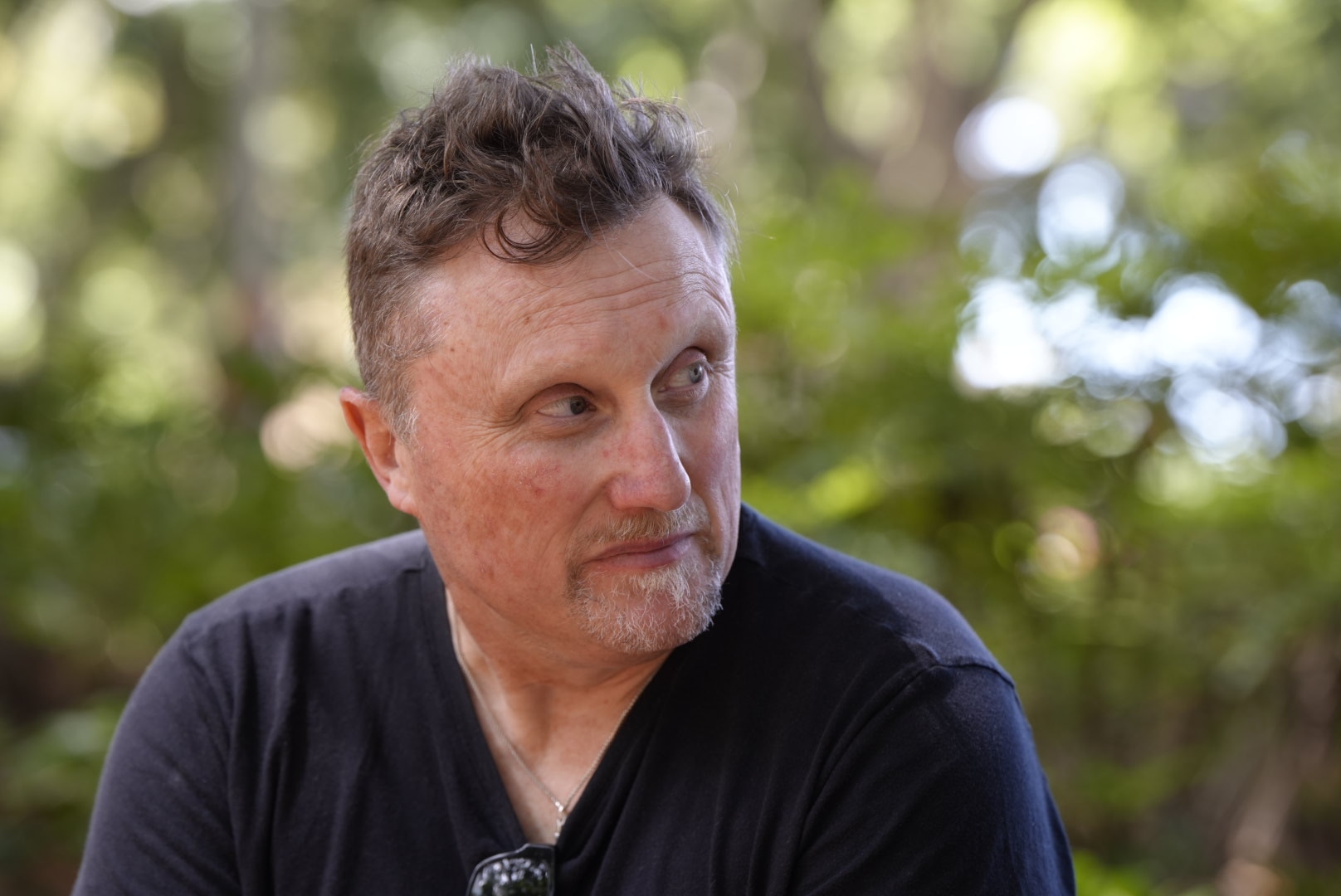 Adam Watts up close, trees behind him, wearing a black shirt.