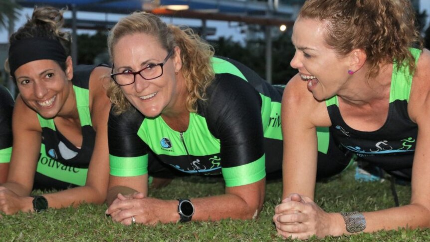 Three women in lycra smiling as they plank in the grass.