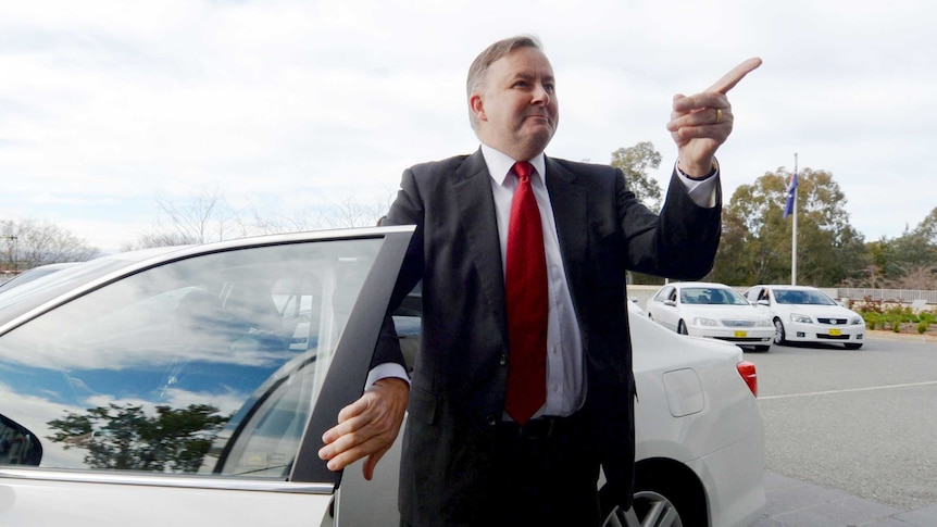 Anthony Albanese points to the sky next to a car