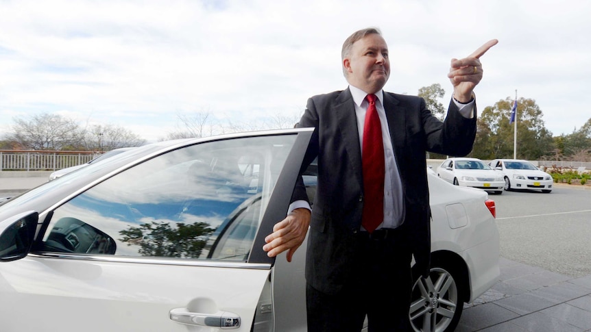 Anthony Albanese points to the sky next to a car
