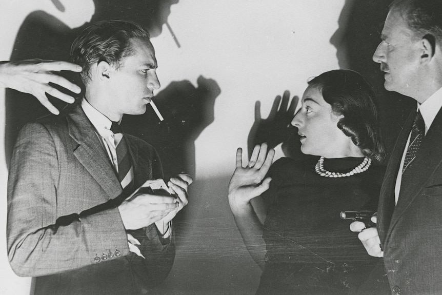 Black and white photo of a man lighting a cigarette, a woman holding her hands up, a man holding a gun. Hand reaching into shot.