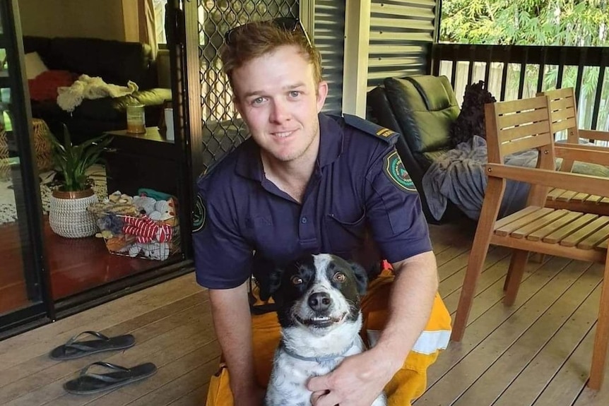 A man in a Queensland firefighters uniform kneeling down with a dog