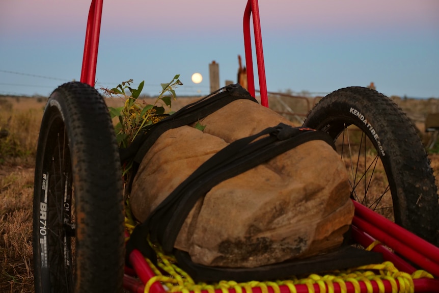 A large rock tied to a buggy with a full moon in the background.