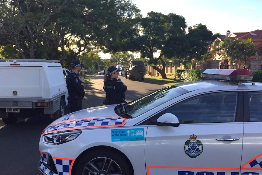 Police officers stand next to a police car which is blocking off a suburban street.