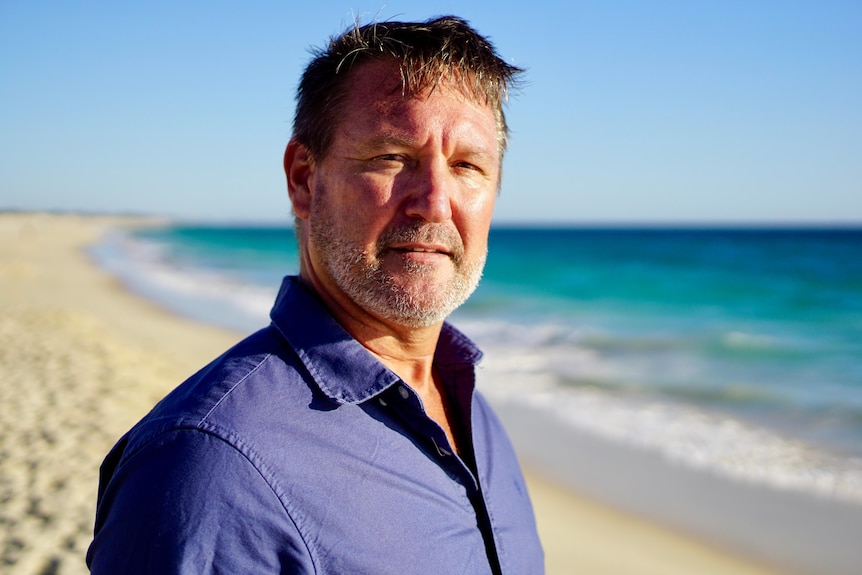 A man wearing a blue shirt, standing on a beach.