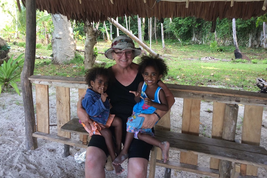Joy Price holding two local children on her lap under a hut.