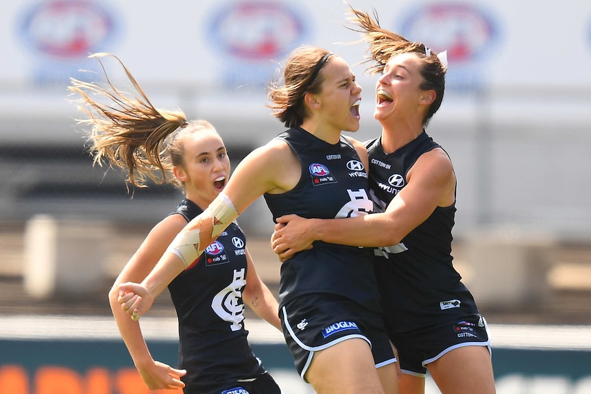 Serena Gibbs celebrates with her mouth open as two teammates in dark blue singlets jump with their mouths open next to her