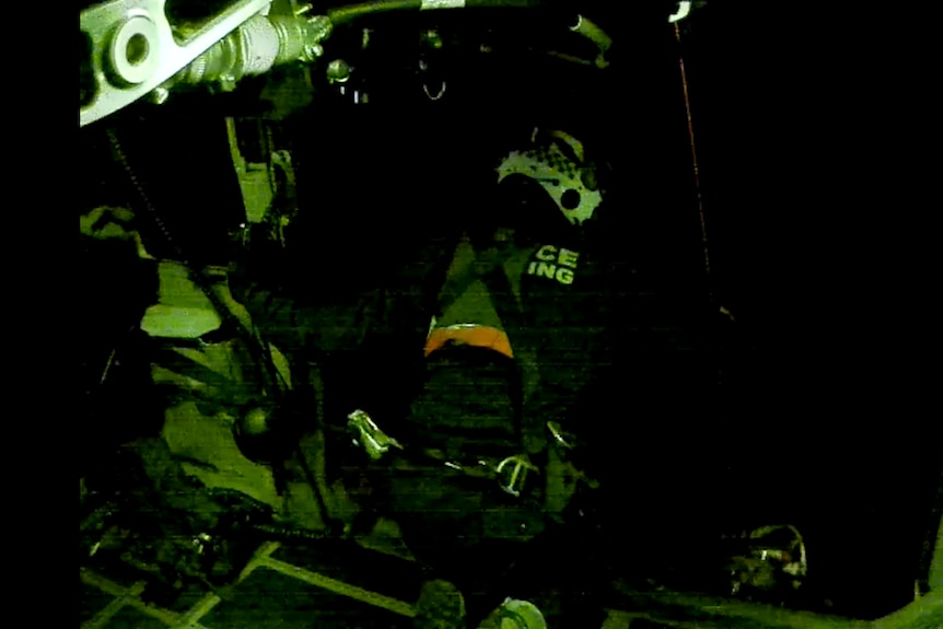 a person wearing a helmet with police wing on his back knees on the edge of the helicopter reaching out to help