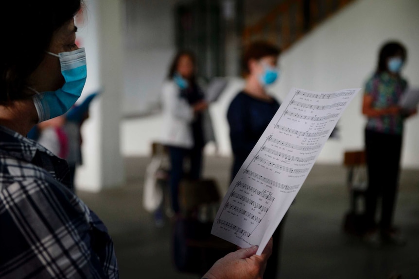 A choir singer wears a mask and holds a sheet of music