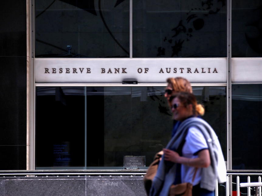 Two  women walk past the Reserve Bank of Australia headquarters, with the building's name prominent in the background.