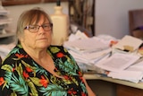 Perth nurse Linda Schmidt sitting at her desk in front of a mound of paperwork