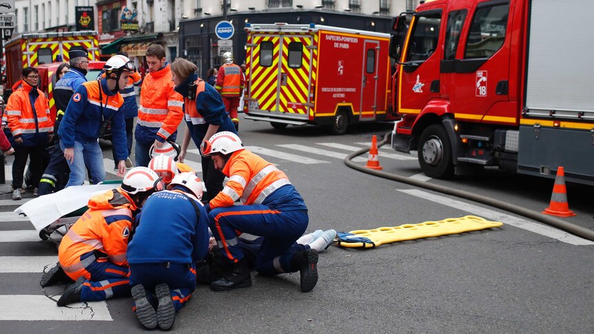 A group of rescuers tend to a wounded person on an intersection in central paris, surrounded by two ambulances and a firetruck.