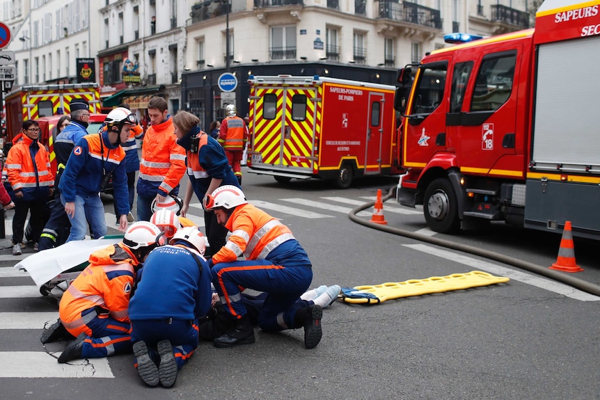 A group of rescuers tend to a wounded person on an intersection in central paris, surrounded by two ambulances and a firetruck.