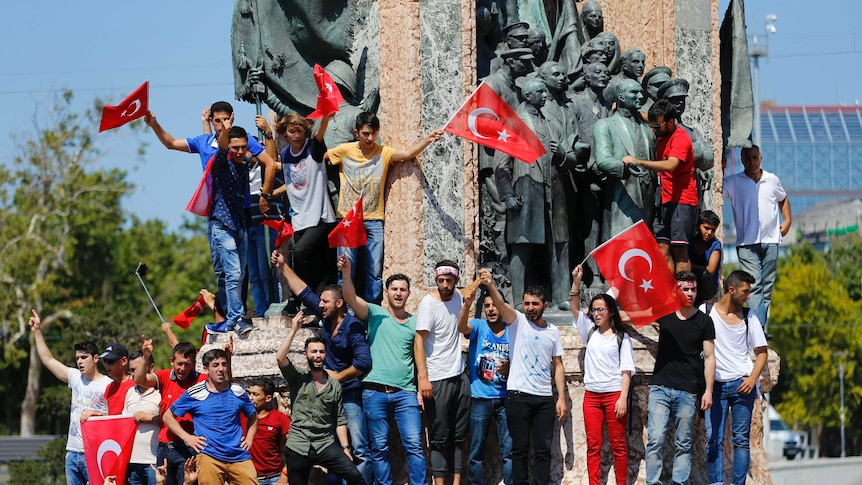 People wave Turkish flags as they stand at a monument in Istanbul.