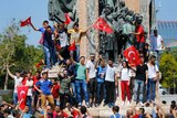 People wave Turkish flags as they stand at a monument in Istanbul