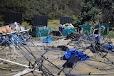 A graveyard of gazebo frames and camping gear littering the ground in front of skips used to keep the beach clean