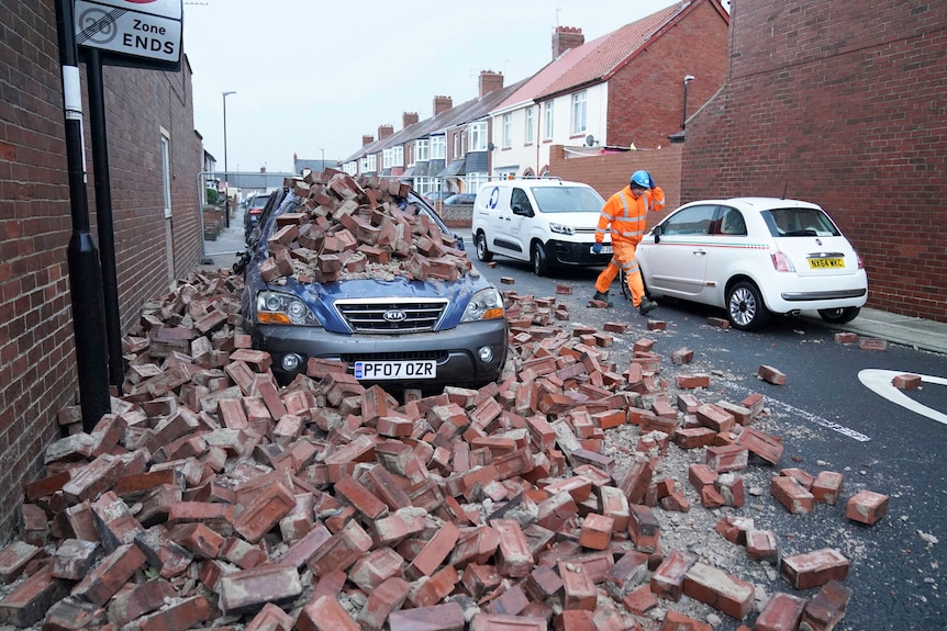 A blue car lies under a pile of bricks