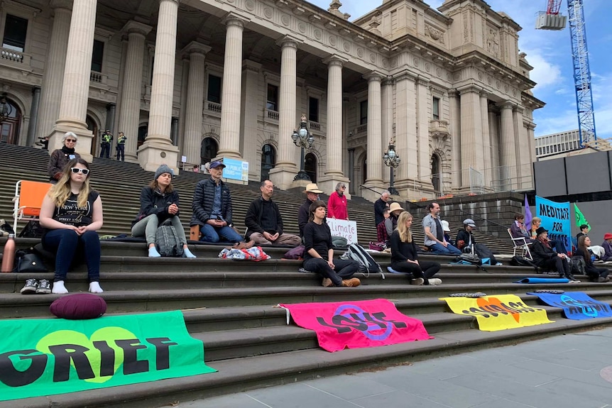 Climate activists sit peacefully on the steps of the Victorian Parliament.