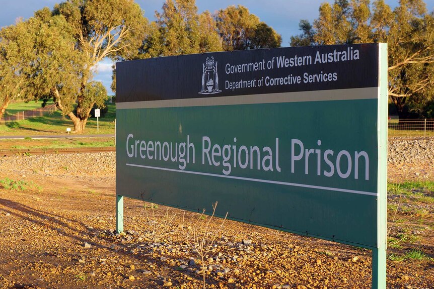 A large sign reading Greenough Regional Prison stands near a road in front of trees.