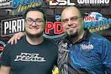 Australian father-son darts duo Ky and Ray Smith smiling for a photo with their arms around one another