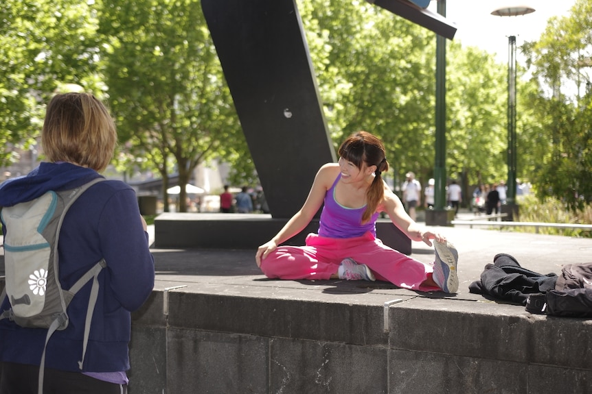 Amy Han smiles and stretches in front of the Melbourne museum as a woman looks on