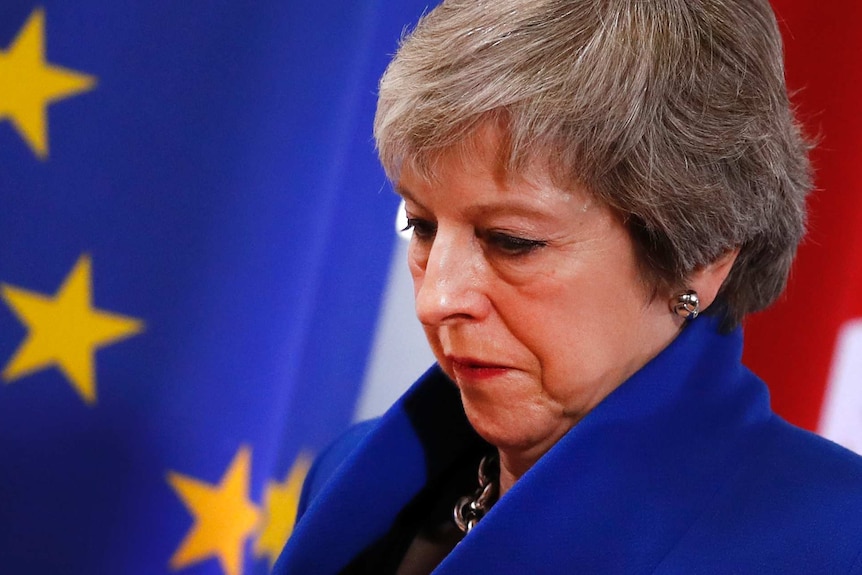 A downcast looking Theresa May with an EU flag in the background