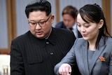 A North Korean man in glasses and a black suit with a North Korean woman in a grey suit