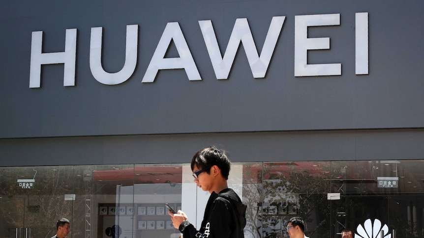 A man looks at his phone as he walks past a Huawei retail store during the day