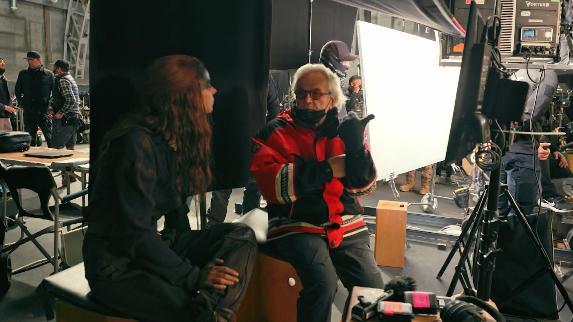 Director George Miller, dressed in a red jacket, directs actress Anya Taylor-Joy on the set of Furiosa.