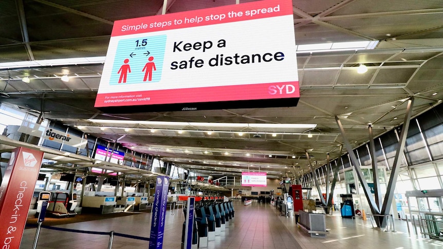 Image of an empty airport terminal with a large social distancing sign.