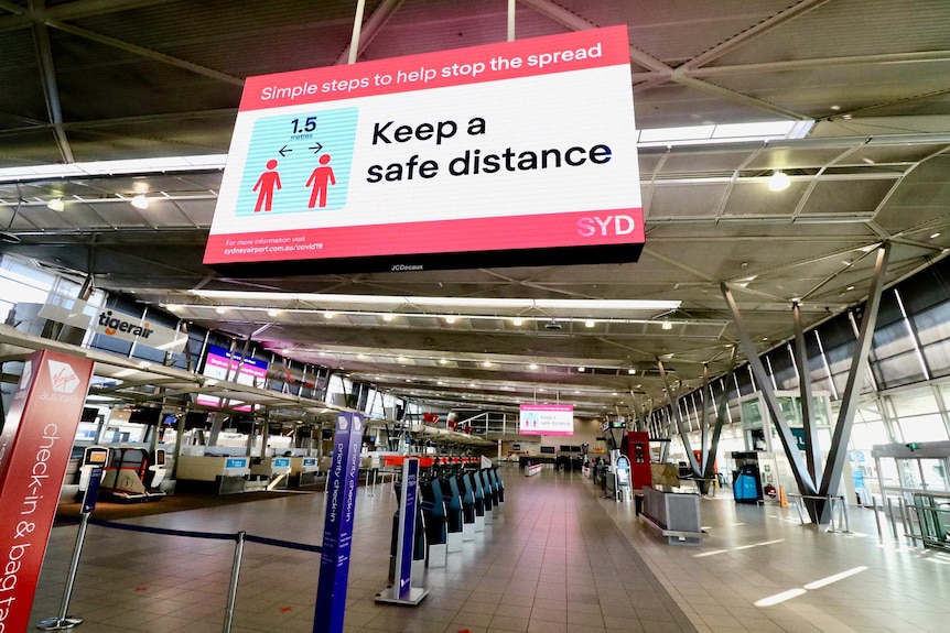 Image of an empty airport terminal with a large social distancing sign.