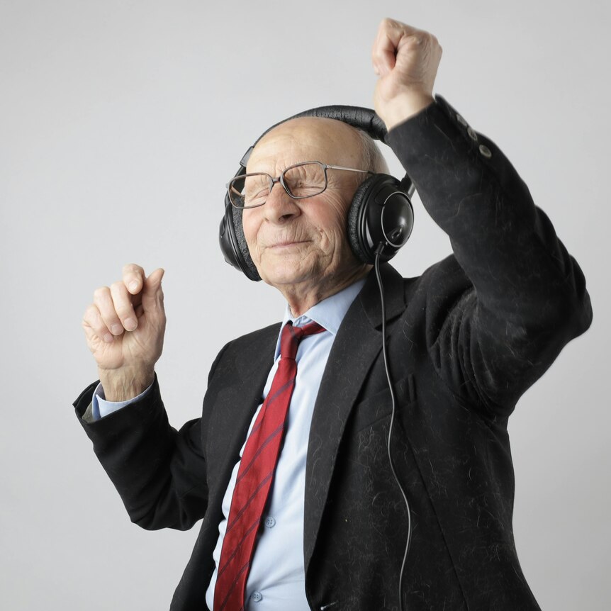 Mid shot of an older man with a bald head, wearing headphones, eyes closed, dancing