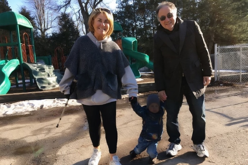 An older couple hold hands with a toddler 