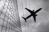 Passenger plane flies over a barbed wire fence as it approaches Sydney airport