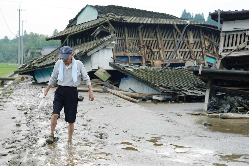 A man walks on a muddy road past homes destroyed by floods.