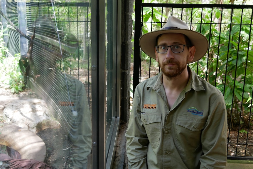Blair Chapman stands in front of a glass enclosure with a baby chimp in the background.