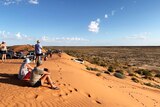 People and four-wheel drive vehicles sit on top on Big Red, the largest sand dune on the edge of the Simpson Desert