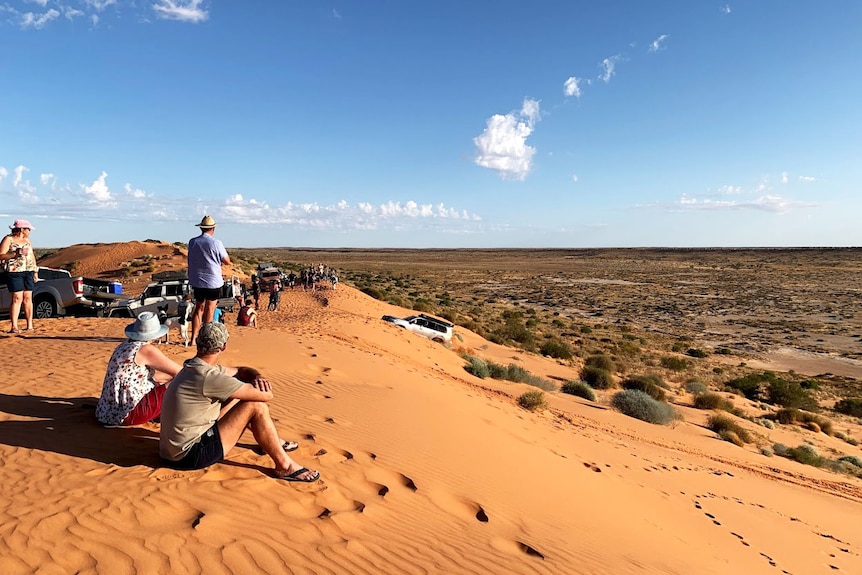 People and four-wheel drive vehicles sit on top on Big Red, the largest sand dune on the edge of the Simpson Desert
